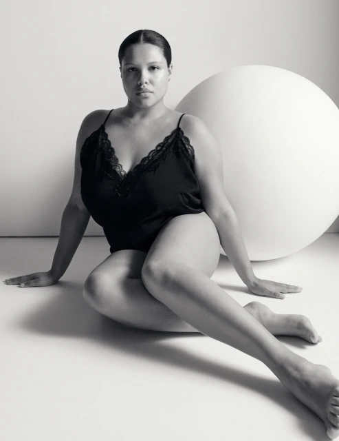 Monochrome studio portrait of a woman in a dark camisole and sitting on the floor, next to a large white sphere.