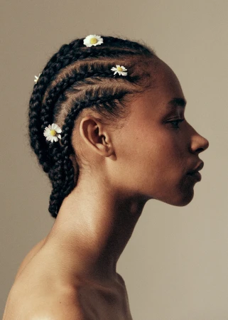 Profile portrait of a black woman with braided hair adorned with small white daisy flowers against a neutral background.