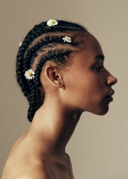 Profile portrait of a black woman with braided hair adorned with small white daisy flowers against a neutral background.