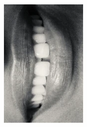 Extreme close-up macro black and white photograph of parted lips revealing white teeth, captured in vertical orientation.