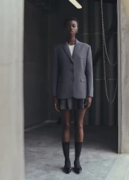 Black woman in a grey blazer and skirt standing indoors by a concrete wall photographed by Rahel Weiss.