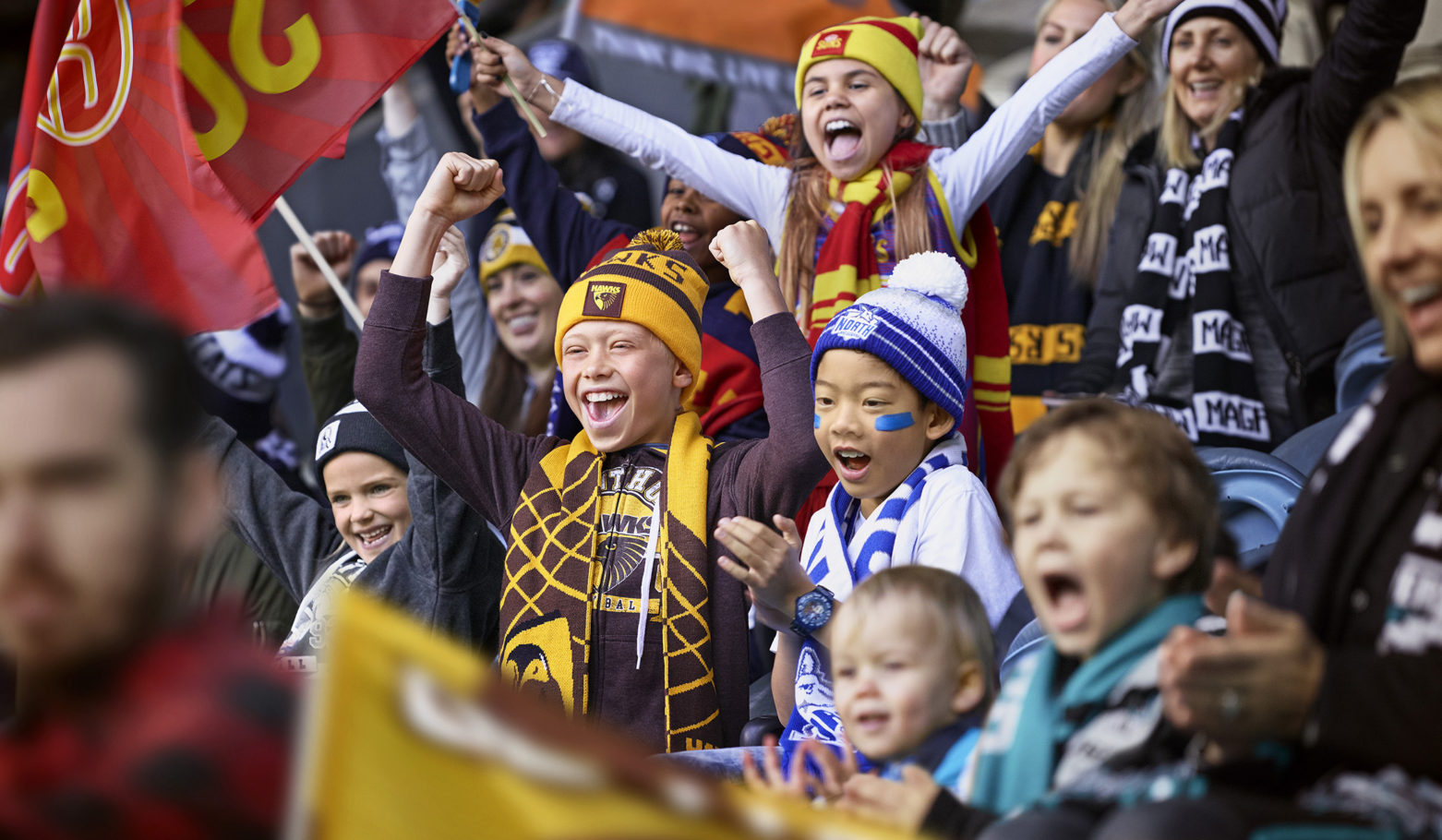 Enthusiastic fans, including children and adults, cheer at an outdoor sporting event, waving flags and showing team spirit with spirited expressions.