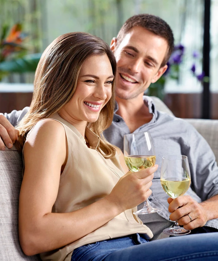 Smiling man and woman holding wine glasses seated together on a sofa photographed by Stuart Crossett