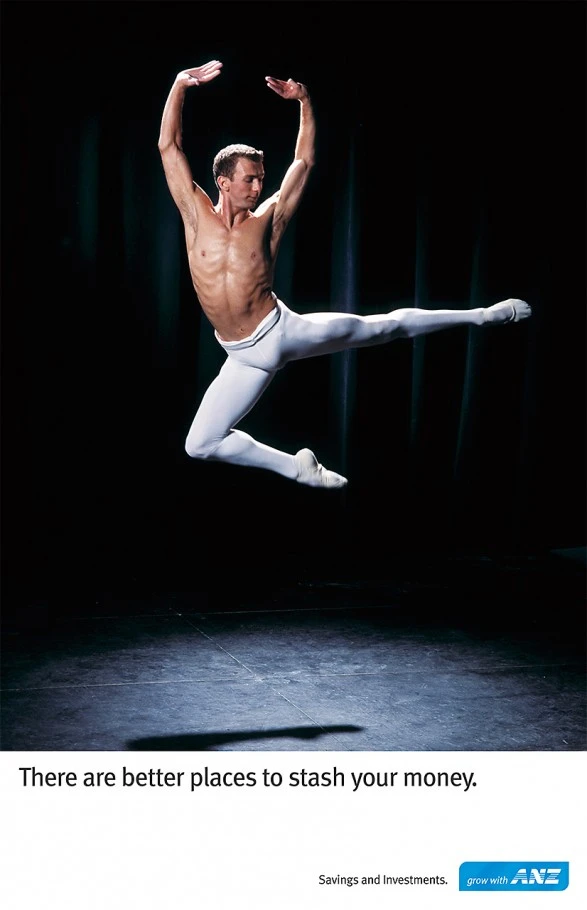 Male ballet dancer leaping mid-air wearing white tights against a dark theatrical backdrop by Stuart Crossett