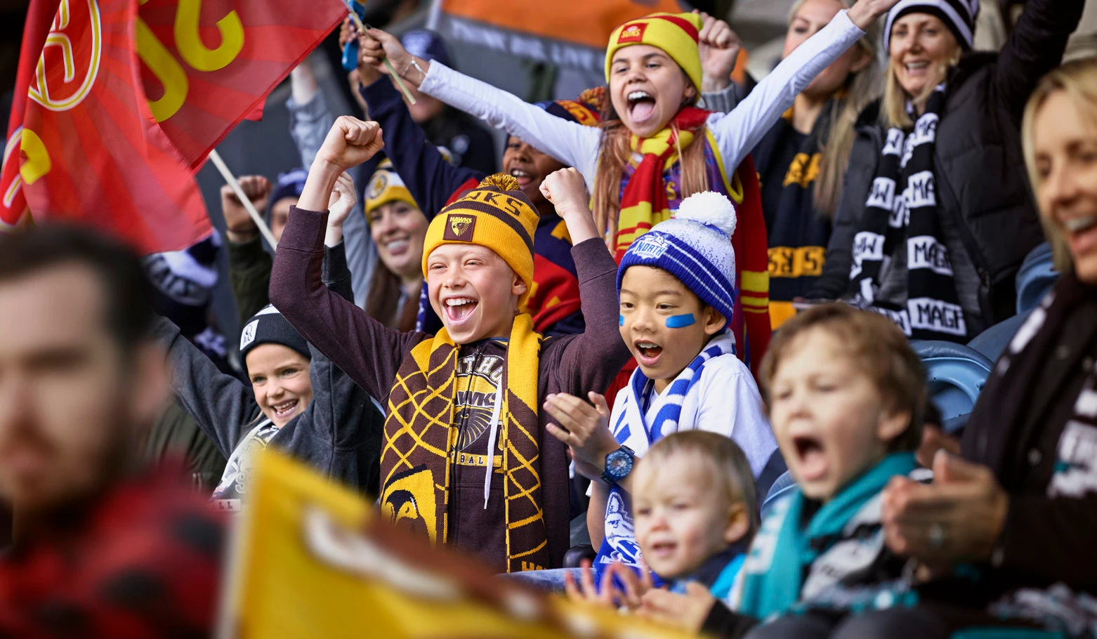 Excited fans in a stadium cheering with scarves and flags, captured by photographer Stuart Crossett in Melbourne.