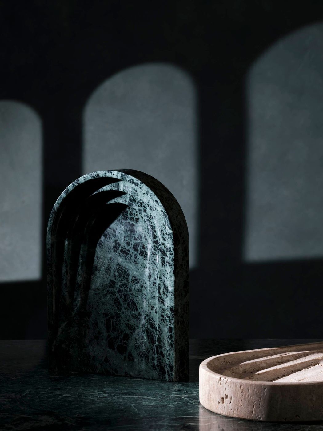 A marble arch and grooved soap dish create an artful still life against a dark gray background with projected arch shadows.