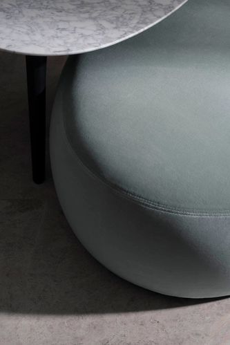 Close-up of a round, light green ottoman with a marble-topped side table, set against a gray marble floor, creating a minimalist interior.