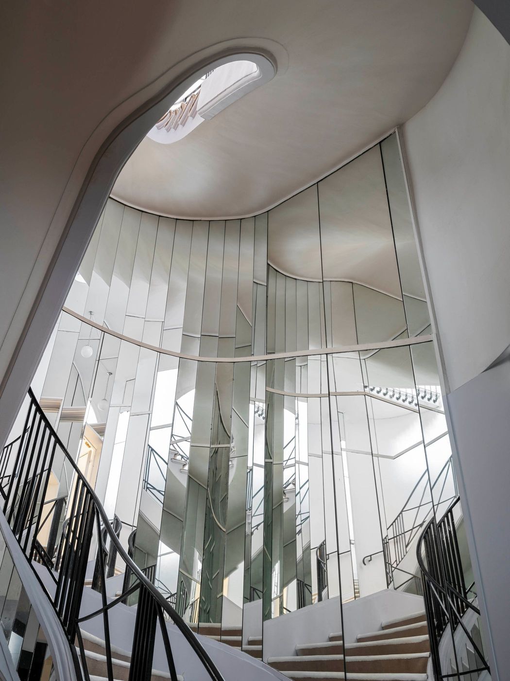 Interior view of a modern staircase featuring mirrored walls and black metal railings, creating a visually dynamic space.