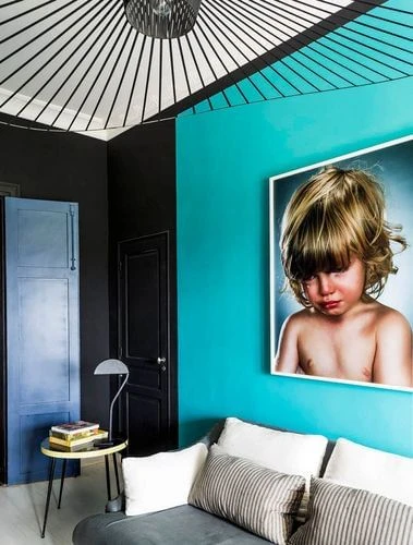 Living room interior with blue and black walls, modern lighting fixture, grey couch, and a framed print of a crying child on the wall.