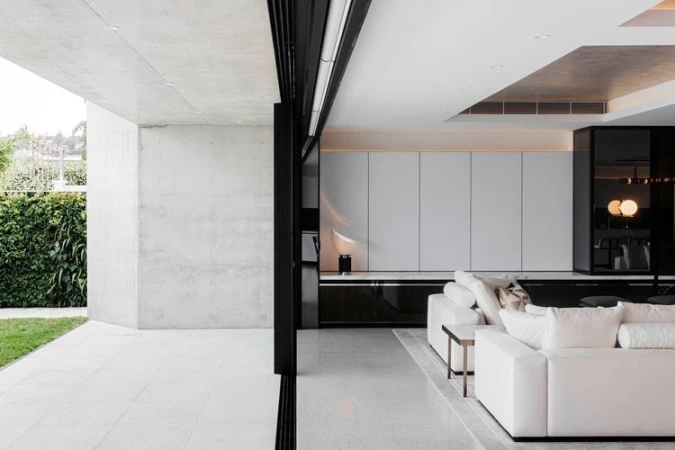 Interior view of modern home featuring white sofa, concrete wall, sliding glass doors opening to a green outdoor space, bright, minimalist design.
