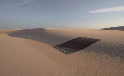 A dark rug rests flat upon undulating sand dunes under a clear pale blue sky, photographed by Felix Forest.
