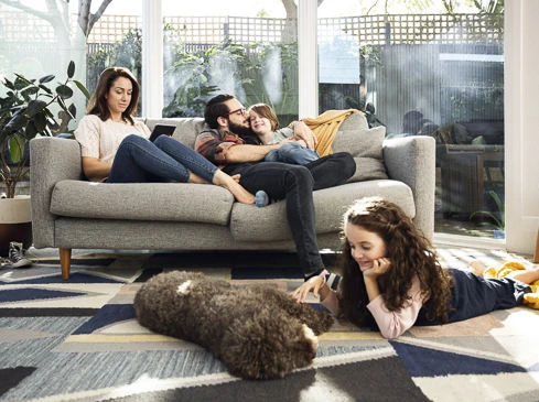 Family relaxes together in a brightly lit living room with their dog, enjoying a comfortable afternoon at home, creating a cozy scene.