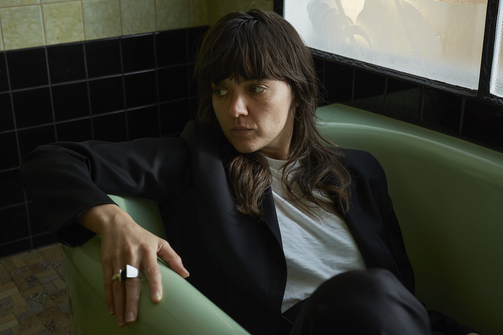 Woman in a black jacket and white t-shirt sitting in a mint green booth with black and white tile in the background.