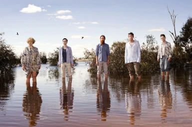 Five people standing waist-deep in shallow water of a reflective lake or flooded landscape under a blue sky.