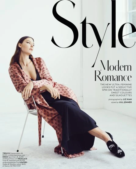 Fashion magazine cover featuring a woman in a pink patterned robe and black dress, seated on a silver chair in a studio setting.