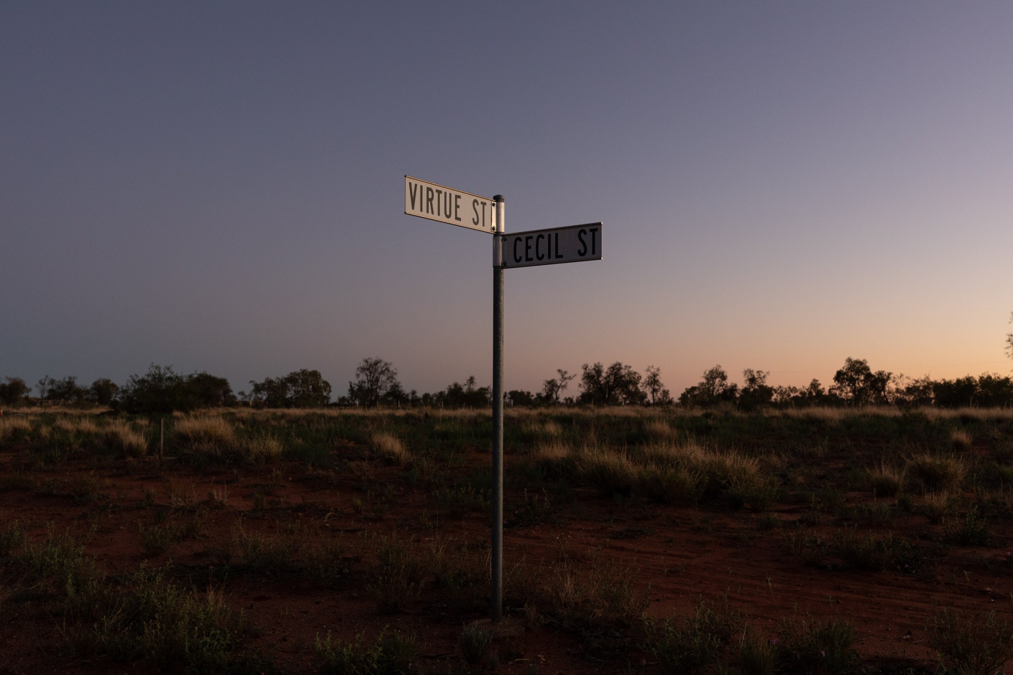 Street sign with 'Virtue St' and 'Cecil St' in a rural setting under a twilight sky. Dirt road in the foreground.