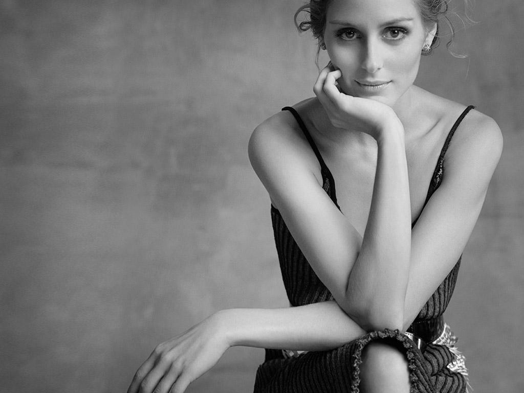 Black and white portrait of a fair-skinned woman with an elegant updo and a thoughtful expression in a studio setting, looking at the camera.