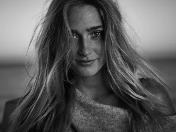 Close-up black and white portrait of a smiling young woman with long loose hair wearing a textured knit sweater.