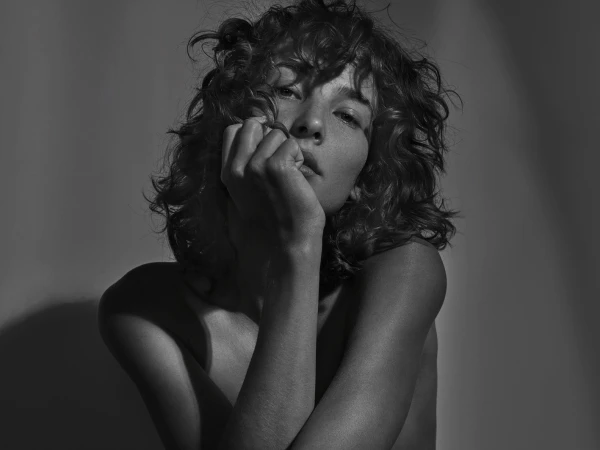Monochrome portrait of a woman with curly hair resting her chin on her hand