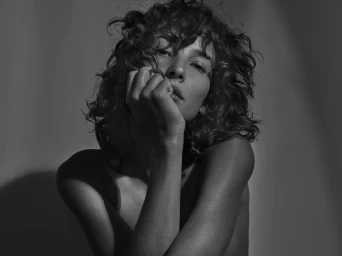 Monochrome portrait of a woman with curly hair resting her chin on her hand