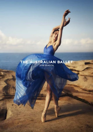 Ballet dancer in a flowing blue dress on rocky coastal rocks with arms raised above her head, photographed by Georges Antoni.