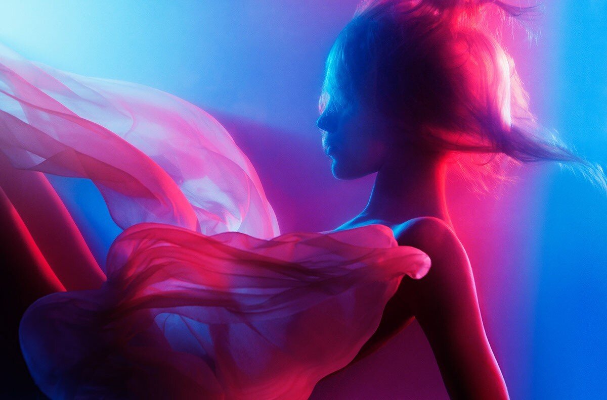 Profile of a woman in flowing pink fabric against a vibrant blue and red gradient studio background