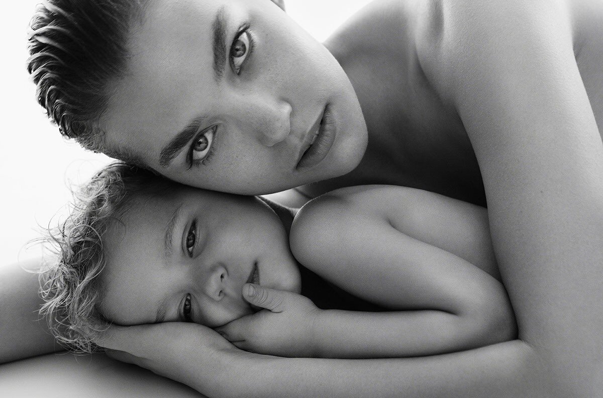 Black and white portrait of a woman and child, faces close together, looking at the camera in a softly lit, intimate studio setting.