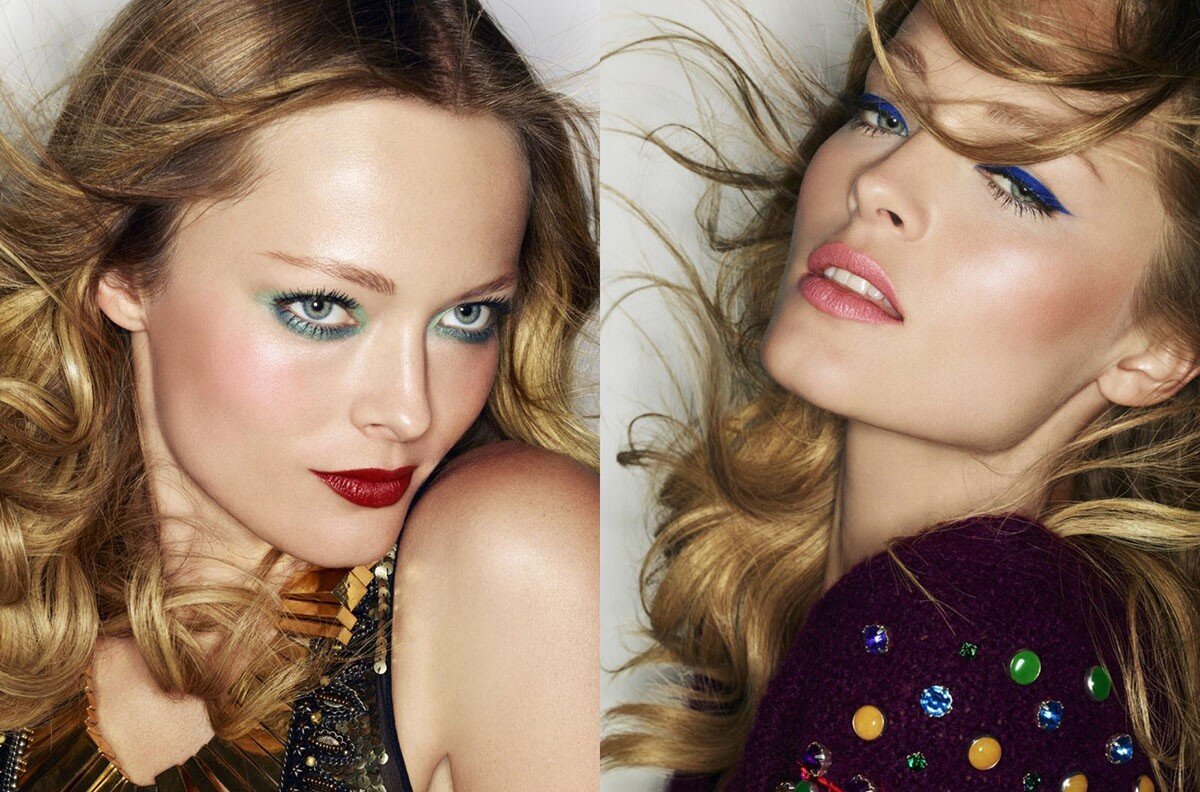 Close-up portrait of two fair-skinned women with long blonde hair, bold eye makeup, and dark lip color, in a beauty editorial.