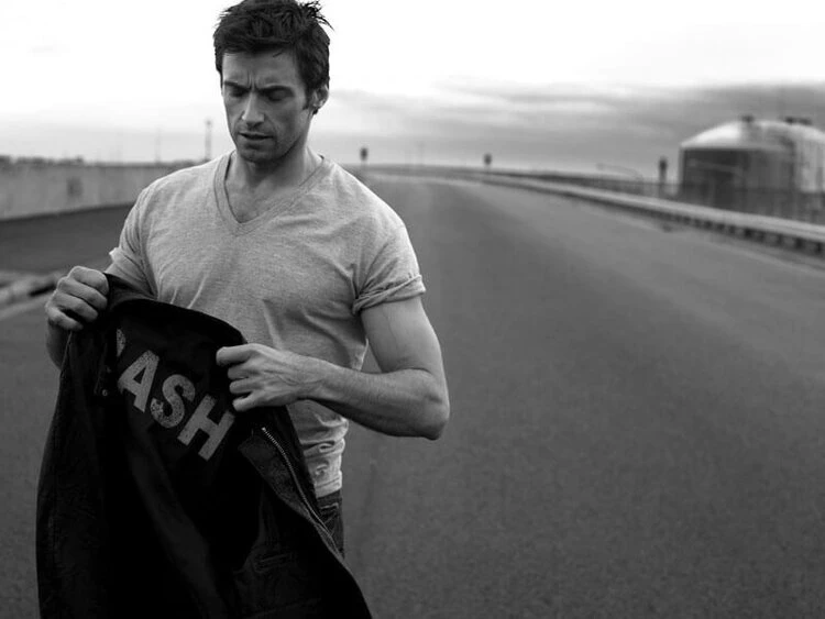 Black and white shot of adult male holding a 'Cash' jacket in an outdoor setting with a road and industrial building visible.