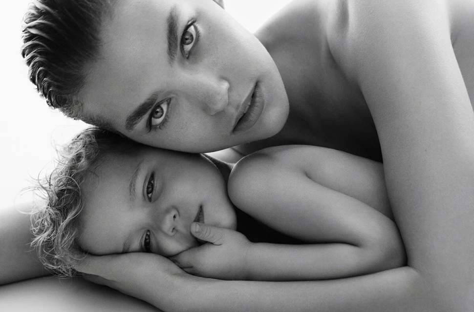 Close-up black and white portrait of an adult holding a young child close against a bright white background.