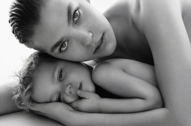 Close-up black and white portrait of an adult holding a young child close against a bright white background.
