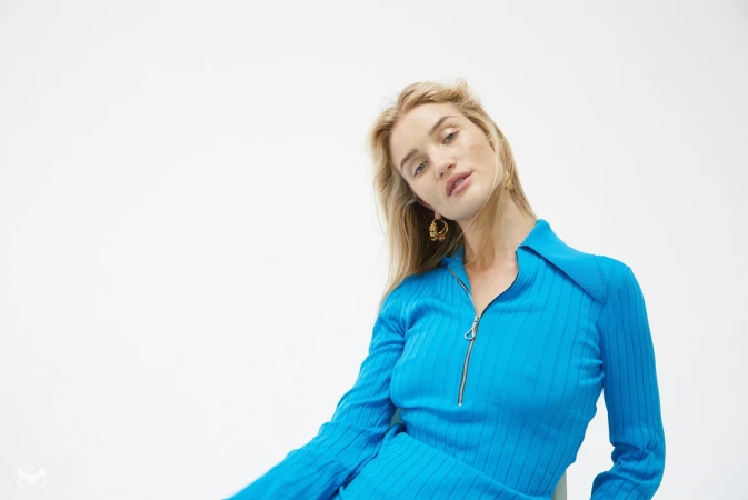 Blonde woman wearing a vibrant blue ribbed zip-top dress with gold hoop earrings against a white background
