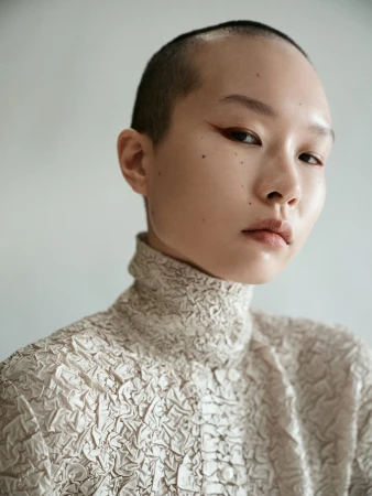 Close up portrait of a person with a shaved head and textured high neck top styled by Nicki Colbran