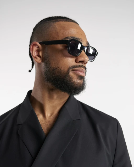 Adult male wearing sunglasses and a black jacket in a studio shot. The man is looking off to the side in a fashion style photo.