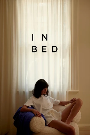 Woman in white shirt and shorts sits in a chair near a window with white curtains in an indoor setting with soft, neutral lighting.