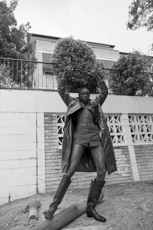 Black and white portrait of a male model wearing a belted coat and tall boots, styled by Nicki Colbran in Sydney.