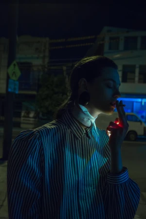 Model in striped shirt and white neck scarf smoking a cigarette at night under street lighting in Sydney