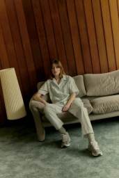 Woman in light blue shirt and trousers seated on a beige sofa against vertical wood panelling in Sydney