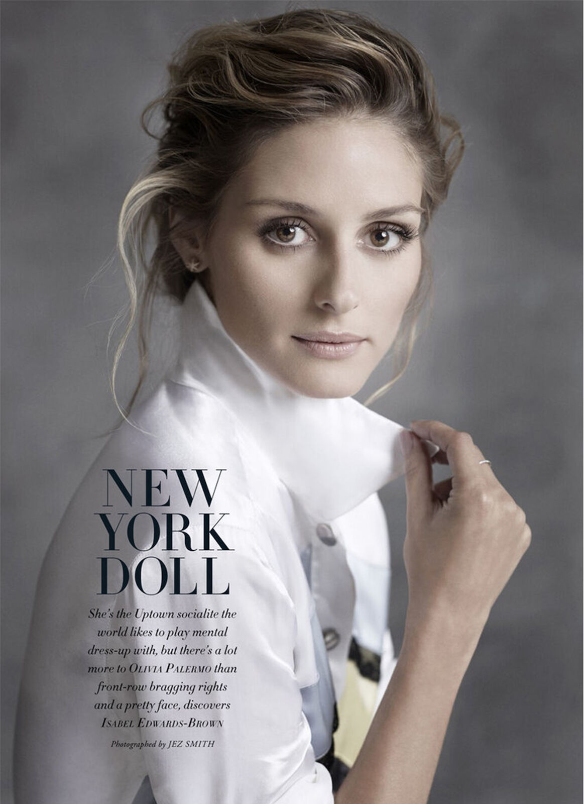Elegant portrait of a stylish woman with blonde hair wearing a white collared shirt, showcasing fashion editorial style against a grey backdrop.