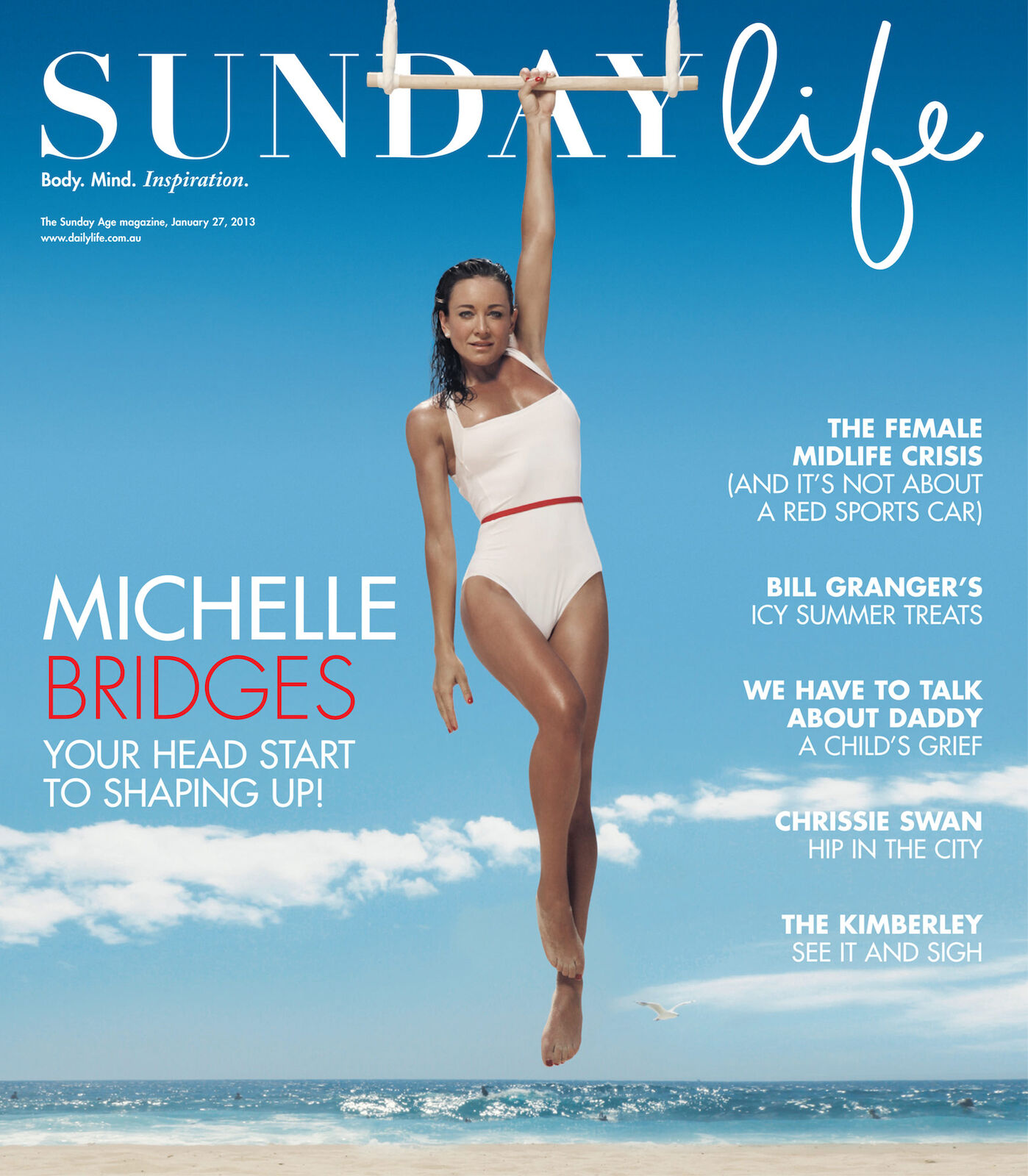 Magazine cover featuring Michelle Bridges in a white swimsuit, hanging from gymnastic rings against a backdrop of ocean and sky.