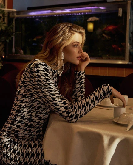 Woman in patterned mini dress poses at restaurant table with teacups in front of a koi fish tank in the background.