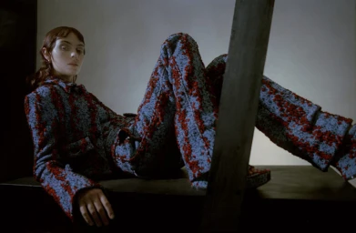 Model wearing patterned blue and red textured suit reclining on a dark surface in a studio setting