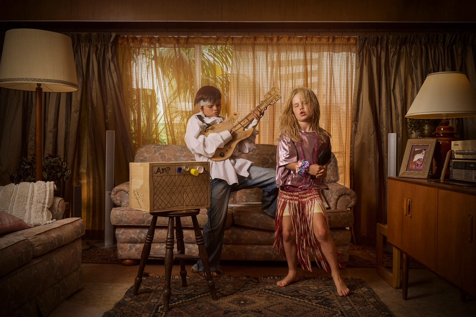 Two children playing rock stars in a living room, boy with toy guitar and girl with hairbrush microphone.