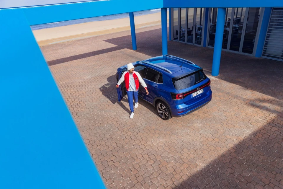 A blue Volkswagen SUV parked outdoors on a brick surface, with a man in a white jacket and blue jeans exiting the vehicle.
