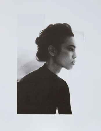 Monochromatic portrait of a young adult woman in profile, wearing a black top and styled hair, against a soft white background.