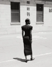 Black woman in a black midi dress standing on an asphalt street in New York photographed by Jenny Kim.