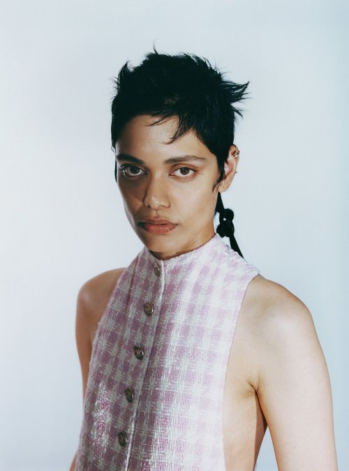Portrait of a person with short dark hair wearing a pink and white patterned sleeveless top against a pale background
