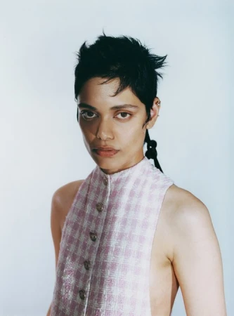 Portrait of a person with short dark hair wearing a pink and white patterned sleeveless top against a pale background