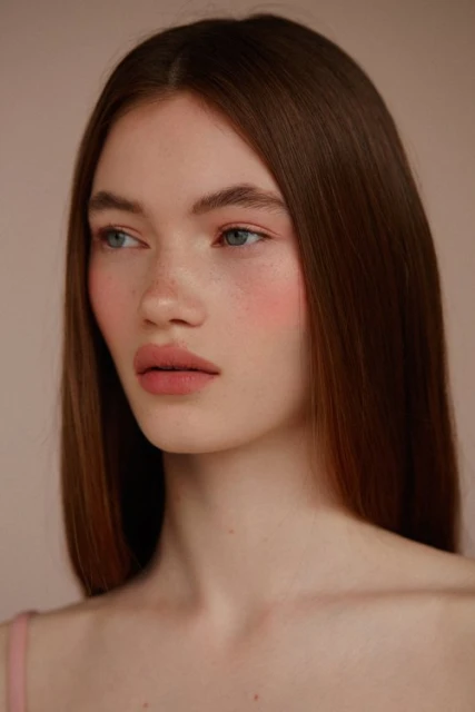 Close-up portrait of a young adult female with auburn hair and light skin, looking off to the side against a neutral background.