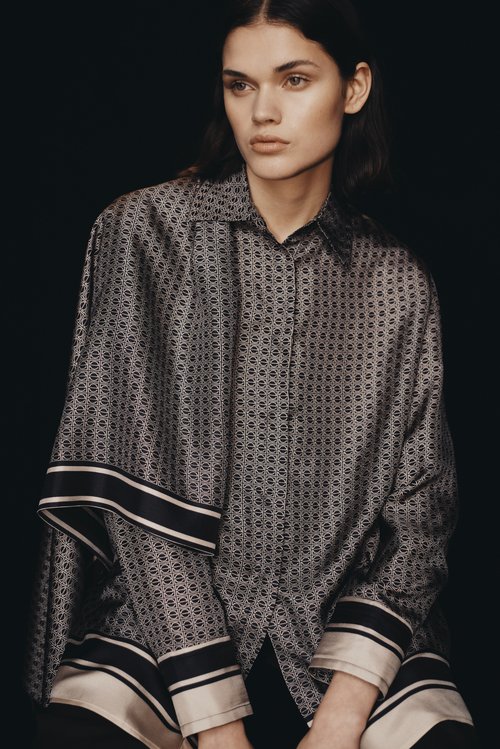 Model wearing a patterned silk shirt with striped cuffs against a dark background, styled by Nisha Van Berkel